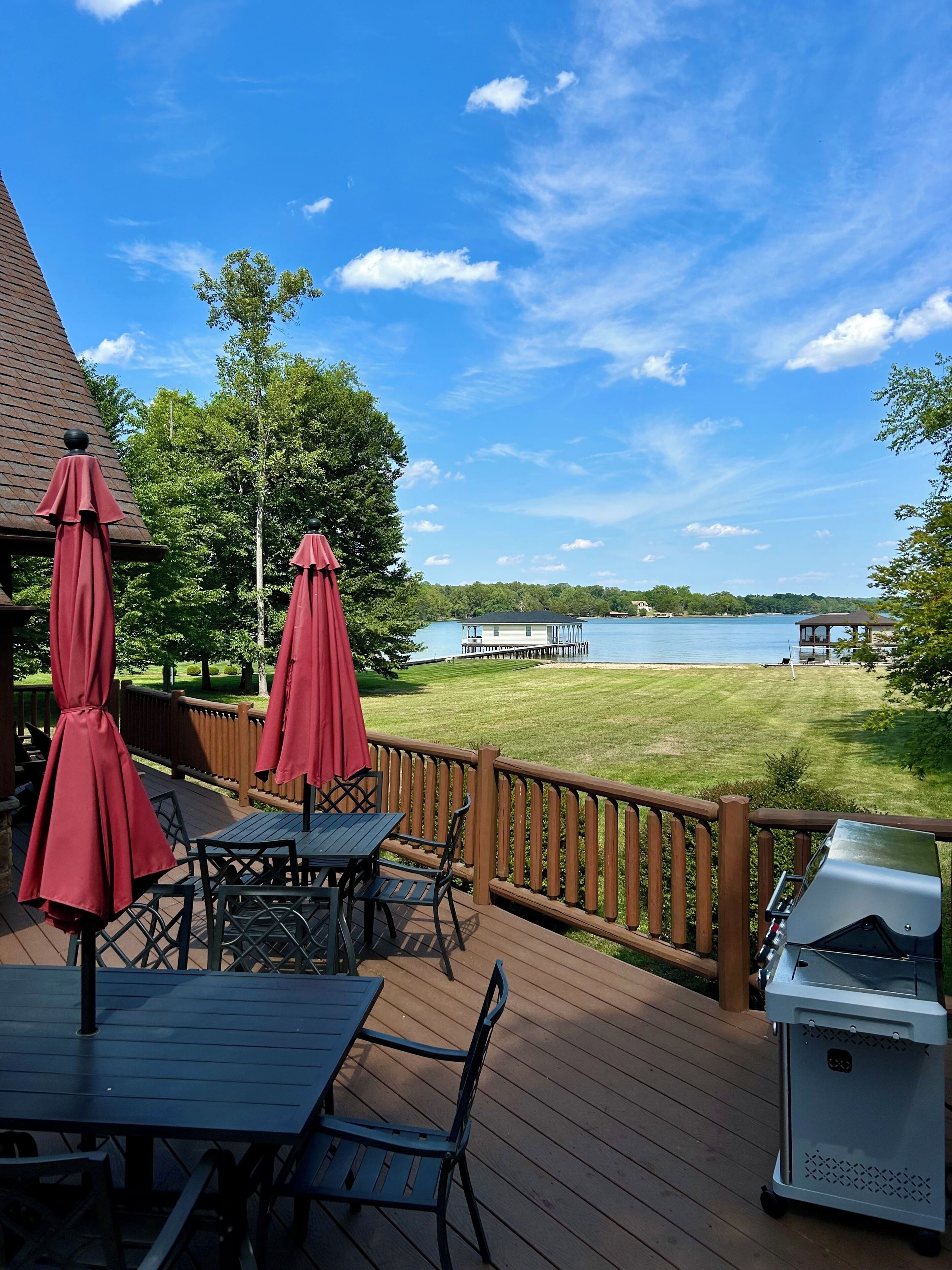 A deck with outdoor seating, a grill, and a view of a lake with a pier.