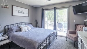 A bedroom with a bed, a desk, a chair, a TV, and a sliding glass door leading to an outdoor area. - Charming Lake House within Walking Distance from Lake (Yankton)