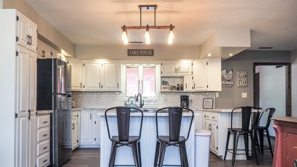 A kitchen with white cabinets, a stainless steel refrigerator, a central island with two chairs, and a sign reading "LAKE HOUSE". - Charming Lake House within Walking Distance from Lake (Yankton)