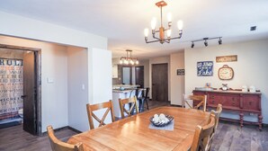 A dining area with a wooden table, chairs, a chandelier, and a kitchen in the background. - Charming Lake House within Walking Distance from Lake (Yankton)