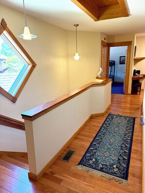 A wooden staircase with a handrail, a blue patterned rug, and pendant lighting.