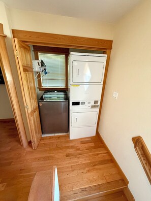 A compact laundry room with a washer and dryer, a small refrigerator, and a window with blinds.