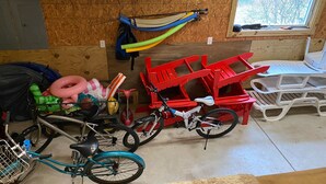 A room with a wooden wall, a window, a bicycle, a red chair, and a white table. - Escape to the Beech House: A Wooded Family- Friendly Retreat Close to the Beach! (Kitty Hawk)