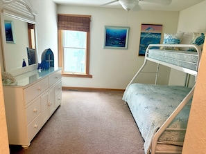 A bedroom with a bunk bed, a dresser, a window with blinds, and two wall-mounted pictures.
