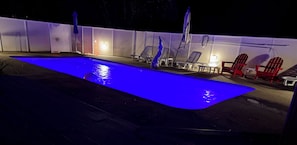 A swimming pool with a blue light, surrounded by lounge chairs and umbrellas.