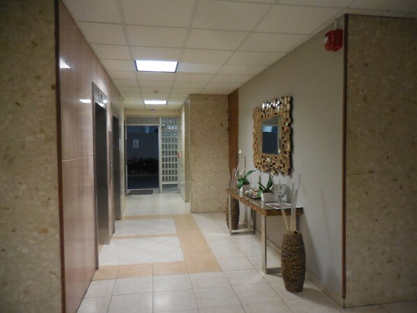A hallway with a tiled floor, a reception desk with a mirror and plants, and a door with a number 5 sign.
