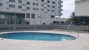 Una piscina al terrat amb una escala metàl·lica, envoltada per una tanca blanca, i un edifici modern al fons.