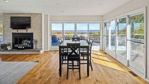 A spacious dining area with a fireplace, large windows, and a view of the outdoors. - Panoramic lake view retreat with firepit! Centrally located on Wine Trail! (Penn Yan)
