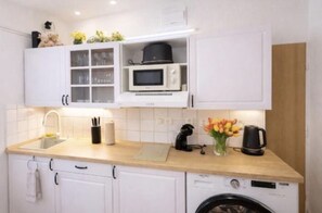 Une cuisine compacte dotée de meubles blancs, d’un four à micro-ondes, d’une machine à café et d’un lave-linge.