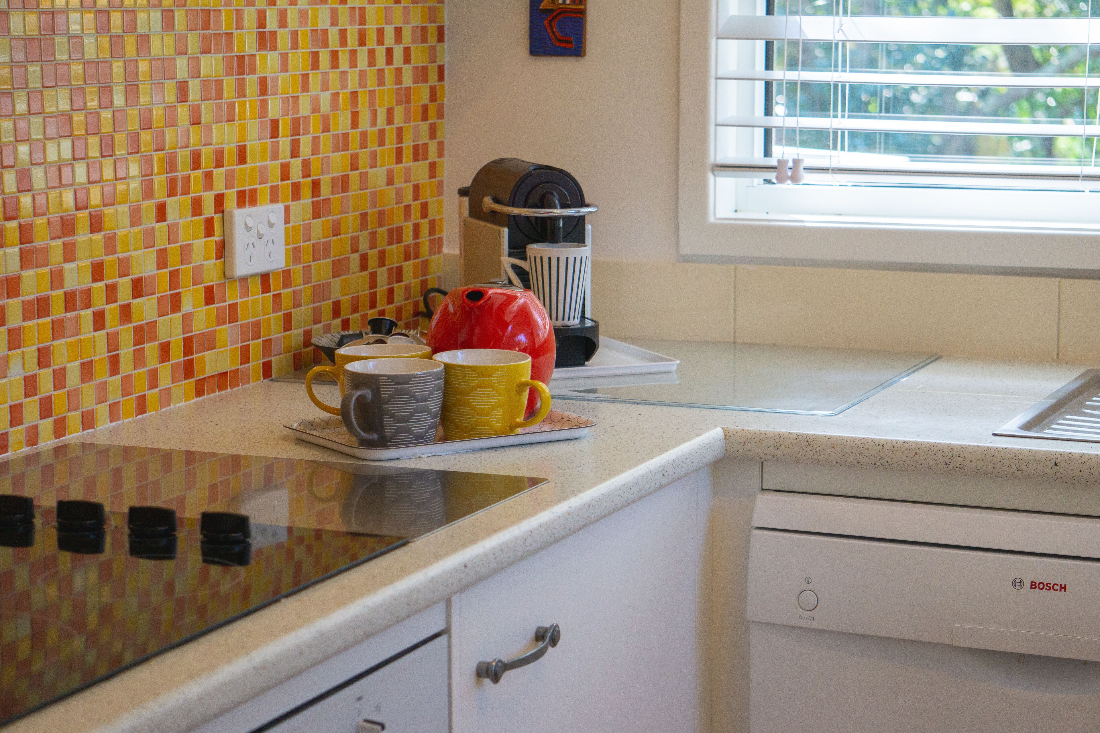 A kitchen with a tiled backsplash, a coffee maker, and a window with blinds.