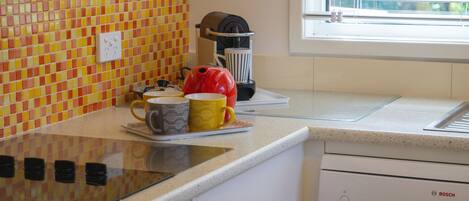 A kitchen with a tiled backsplash, a coffee maker, and a window with blinds.