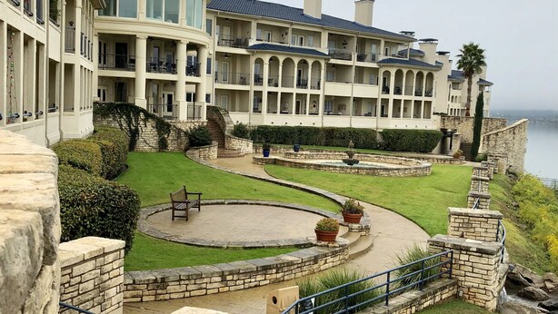 A large, multi-story building with a prominent dome and arched windows, surrounded by a well-maintained garden and a stone wall. - STUNNING views of LAKE TRAVIS @ The Island (Lago Vista)