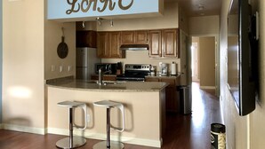 A kitchen with wooden cabinets, a central island with stools, a hanging sign above the island, and a microwave. - STUNNING views of LAKE TRAVIS @ The Island (Lago Vista)