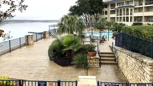 A hotel pool area with a view of the water, stone steps, and a building with balconies. - STUNNING views of LAKE TRAVIS @ The Island (Lago Vista)