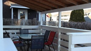 Eine überdachte Terrasse mit Tisch und Stühlen, ein weißer Zaun und Blick auf die Nachbarschaft.