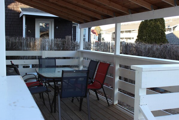 A covered patio with a table and chairs, a white fence, and a view of the neighborhood.