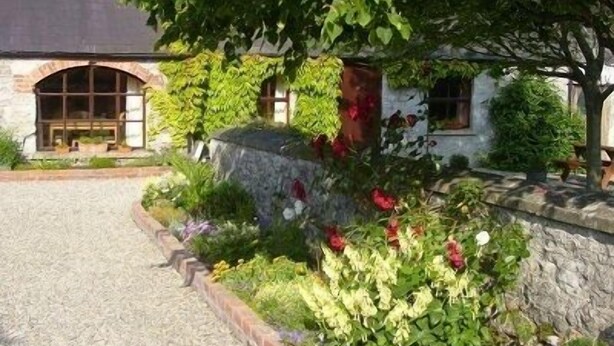 A stone building with a gravel driveway, surrounded by a garden with various plants and flowers. -  Charming old-world country cottage, near Adare  (Kildimo)