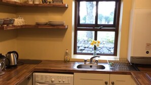 A compact kitchen with a washing machine, a sink, wooden countertops, and shelves with dishes. -  Charming old-world country cottage, near Adare  (Kildimo)