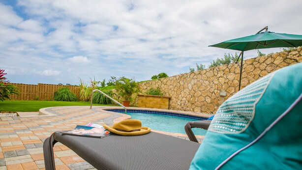 Uma área à beira da piscina com espreguiçadeira, chapéu e guarda-sol.
