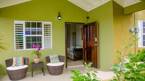 Um quarto com parede verde, móveis de vime, planta em vaso e porta que dá para outro cômodo.