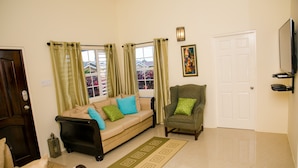 Uma sala de estar com um sofá bege, uma poltrona verde e um tapete estampado.