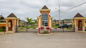 Uma entrada murada com um arco central, cercada por uma cerca e um pequeno jardim.