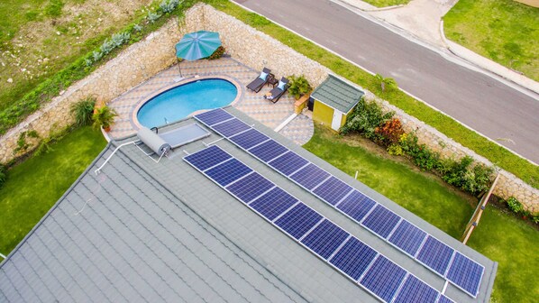 Un toit équipé de panneaux solaires, une piscine et un petit espace jardin agrémenté d’un banc et d’un parasol.