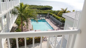A pool with a view of the ocean, surrounded by greenery and a white fence. -  Oceanfront Marina Condo With All Luxuries (Key West)