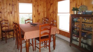 Ein Esszimmer mit Holzpaneelausstattung, einem Esstisch mit sechs Stühlen, einem Deckenventilator und einer Vitrine mit Glastüren.