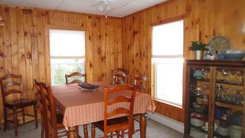 Une salle à manger avec un mur lambrissé en bois, une table à manger entourée de six chaises, un ventilateur de plafond et un buffet aux portes vitrées.