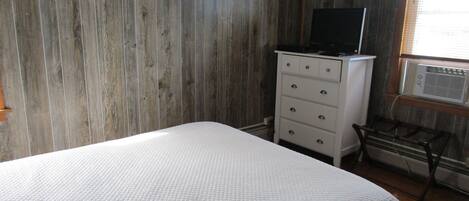 A bedroom with a bed, a dresser, a television on top of the dresser, and an air conditioning unit mounted on the wall.