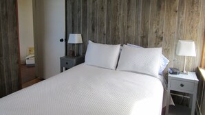 Ein Schlafzimmer mit einer Holzwand, einem Bett mit weißer Bettwäsche, zwei Nachttischen mit Lampen und einer Tür zu einem anderen Raum.