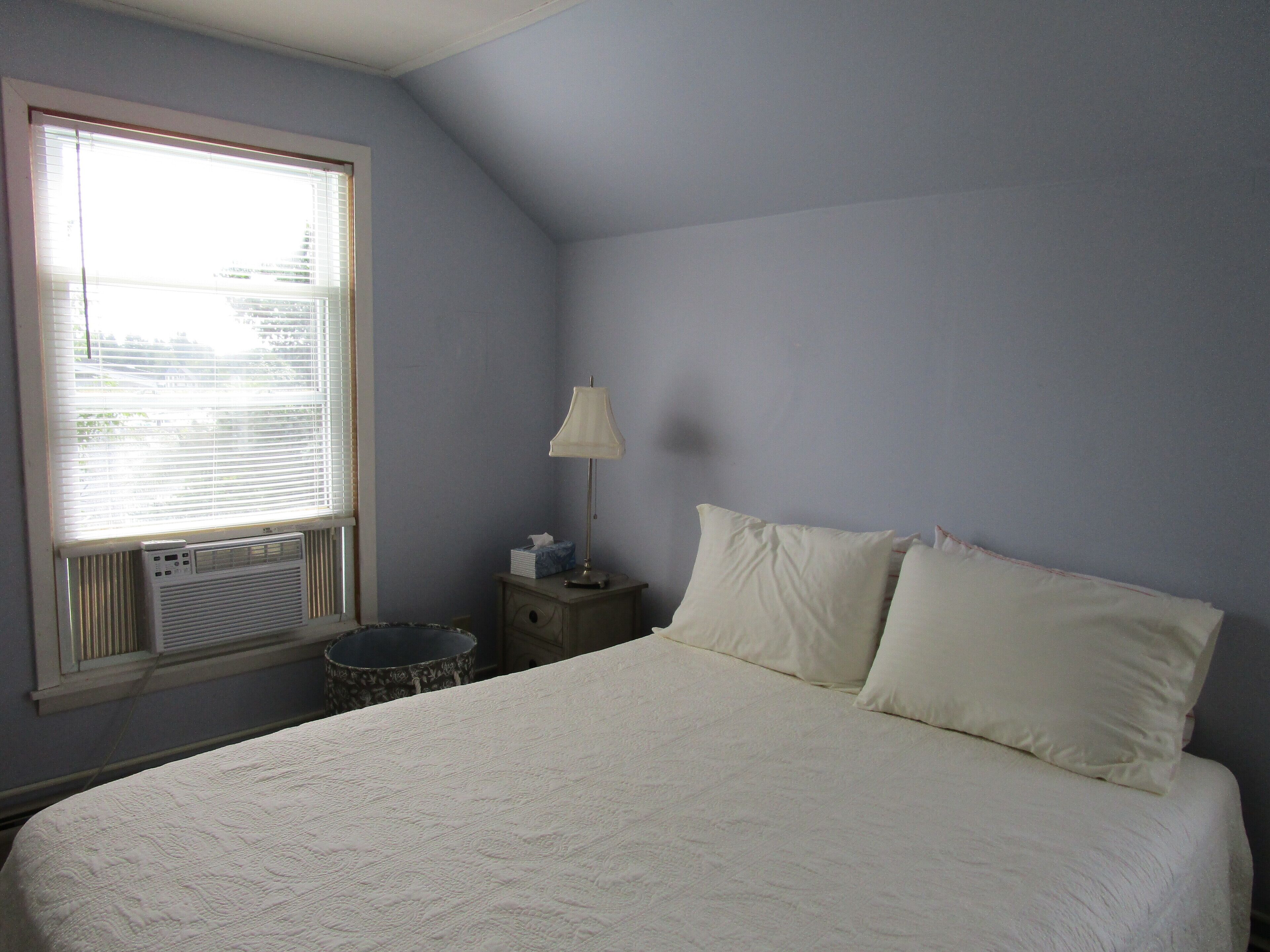 A bedroom with a large bed, a bedside table with a lamp, and a window with blinds.