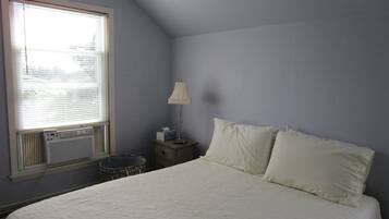 A bedroom with a large bed, a bedside table with a lamp, and a window with blinds.