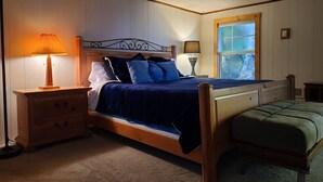 Een slaapkamer met een houten bed, een nachtkastje, een lamp, een raam met uitzicht en een kleine tafel.