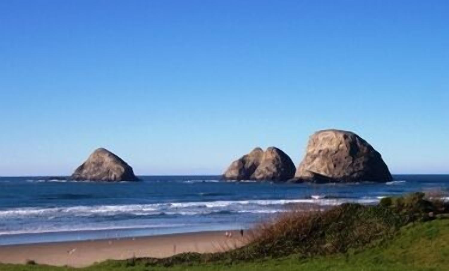 A beach with three large rock formations and a clear blue sky.