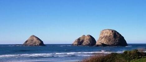 A beach with three large rock formations and a clear blue sky.