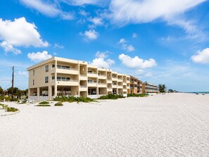A beachfront hotel with multiple floors, balconies, and a sandy beach in the background. - BOUTIQUE BEACH FRONT LUXURY LOCATED DIRECTLY ON BEACH WITH FABULOUS SUNSETS (Bradenton Beach)