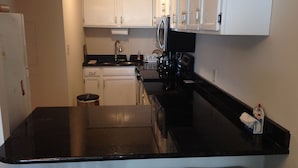 A compact kitchen with white cabinets, a black countertop, and a stainless steel refrigerator. - Direct Oceanfront 2 Bedrm, 2 Bath ATLANTIS Coastal Hwy at 103rd St (Ocean City)