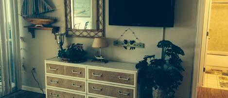 A room with a wooden dresser, a television mounted on the wall, a decorative mirror, and a welcome sign.