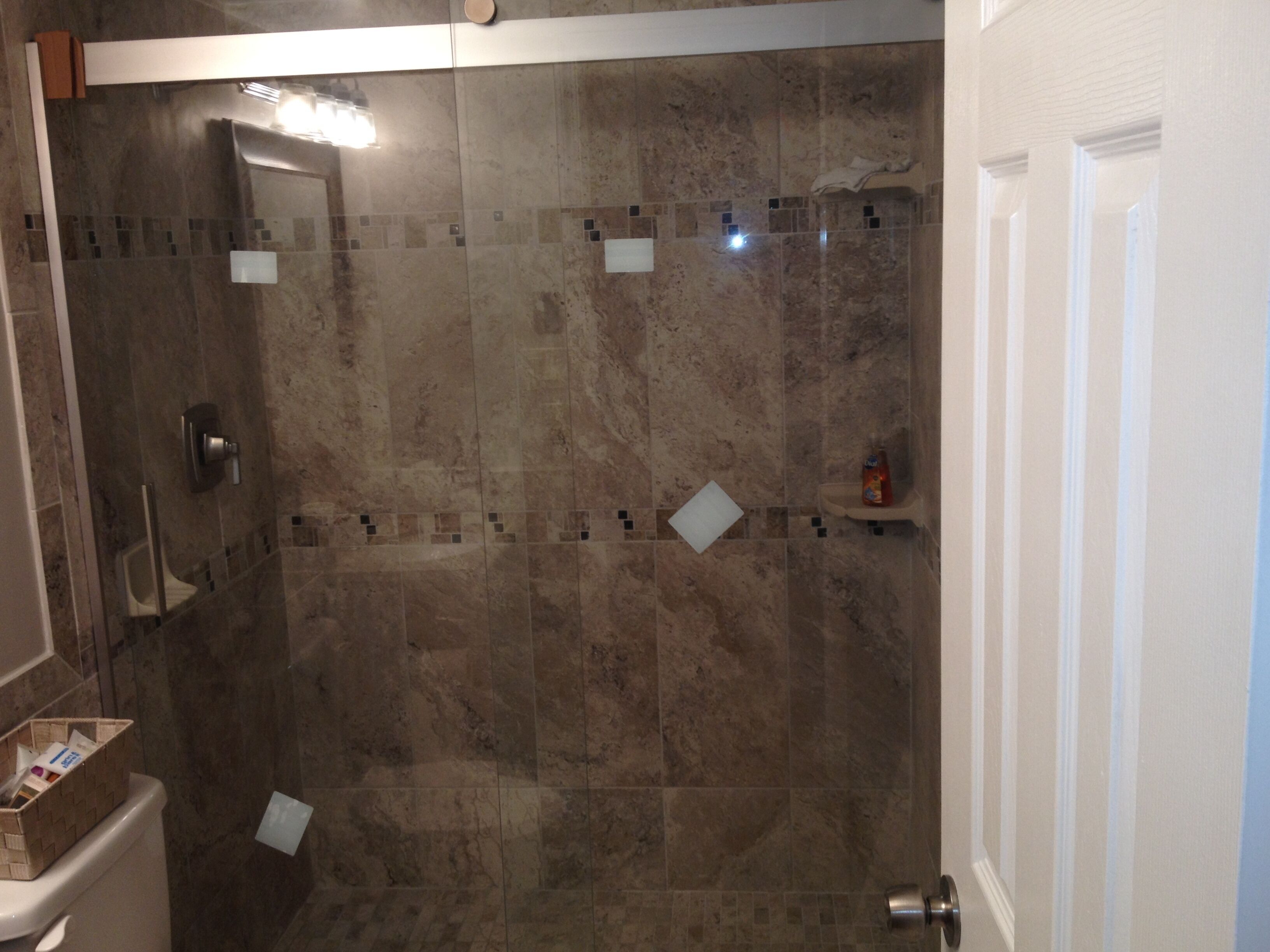 A shower area with a glass door, a towel rack, and a small shelf with toiletries.