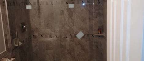 A shower area with a glass door, a towel rack, and a small shelf with toiletries.