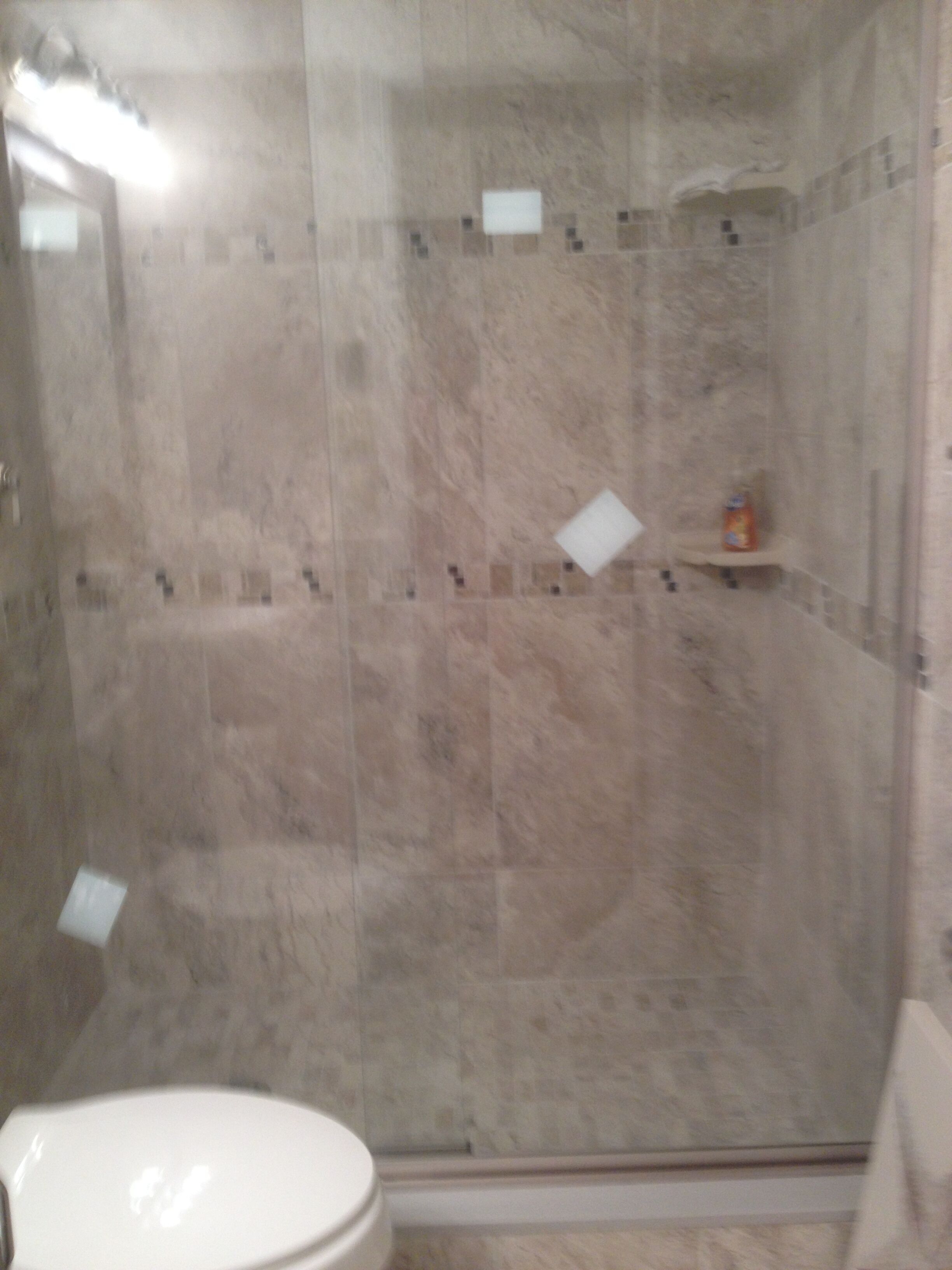 A bathroom with a toilet, a shower area with a glass door, and a tiled wall.