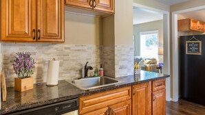 A kitchen with wooden cabinets, a stainless steel sink, and a tiled backsplash. - The Beehive - A charming cottage in the Perry District (Spokane)