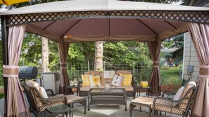 A covered outdoor seating area with wicker furniture, a glass-top table, and a grill. - The Beehive - A charming cottage in the Perry District (Spokane)
