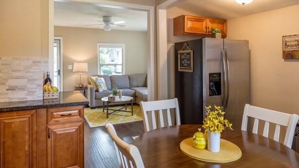 A kitchen with wooden cabinets, a stainless steel refrigerator, a dining table with chairs, and a small rug. - The Beehive - A charming cottage in the Perry District (Spokane)