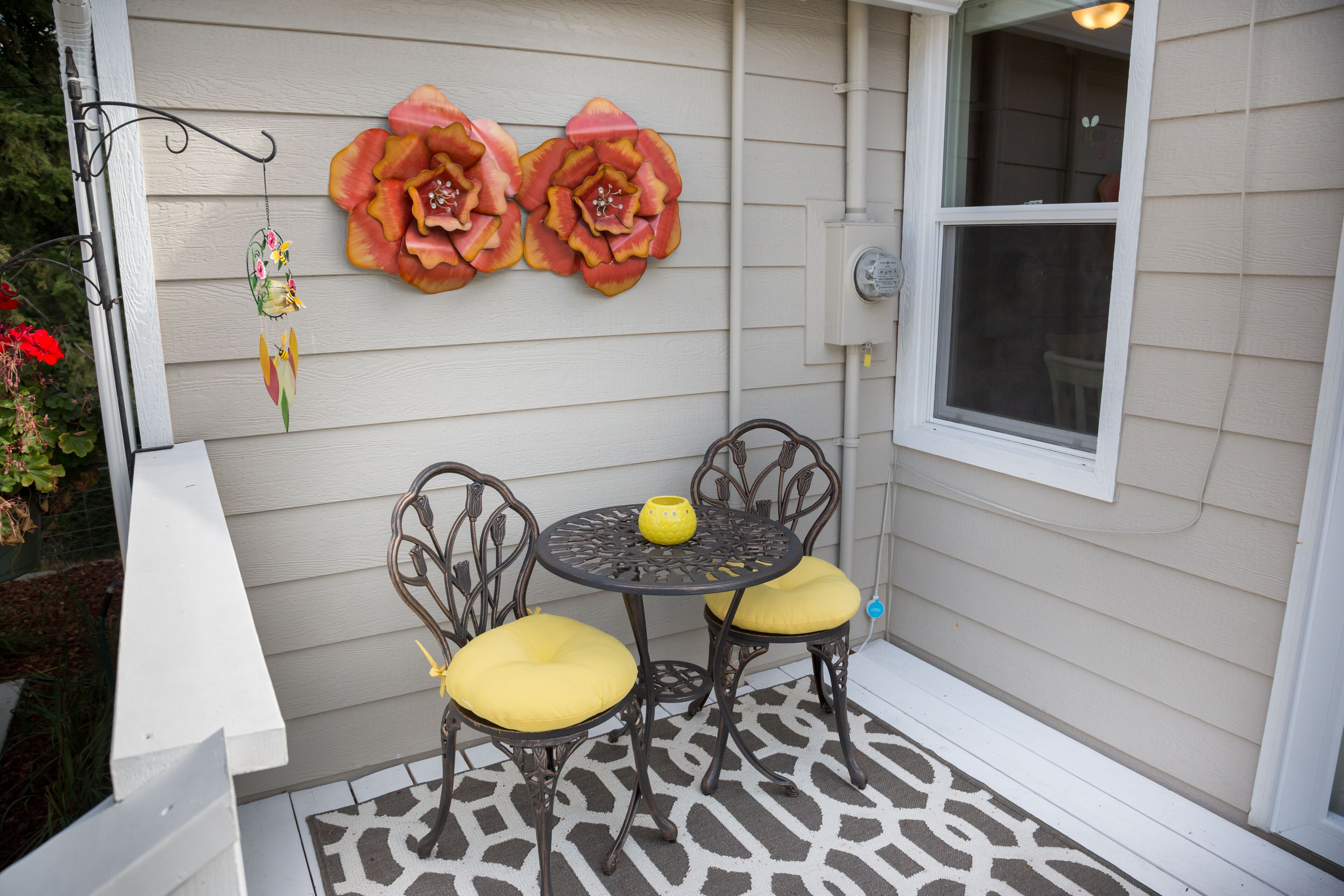 A patio with two chairs and a table, a decorative flower wall, and a window.