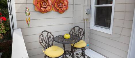 A patio with two chairs and a table, a decorative flower wall, and a window.