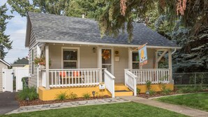 A two-story house with a front porch, a yellow front door, and a flag. - The Beehive - A charming cottage in the Perry District (Spokane)