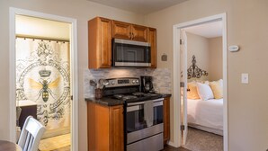 A compact kitchen with wooden cabinets, a microwave, stove, and a coffee maker. - The Beehive - A charming cottage in the Perry District (Spokane)